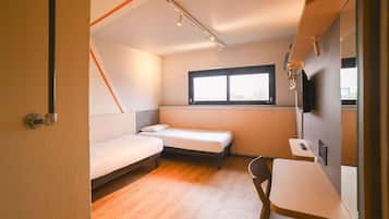 A compact room with a bed, a small table, a chair, a window, and a television.