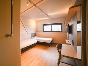 A compact room with a bed, a small table, a chair, a window, and a television. - Ibis Budget Poitiers Site Du Futuroscope (Chasseneuil-du-Poitou)