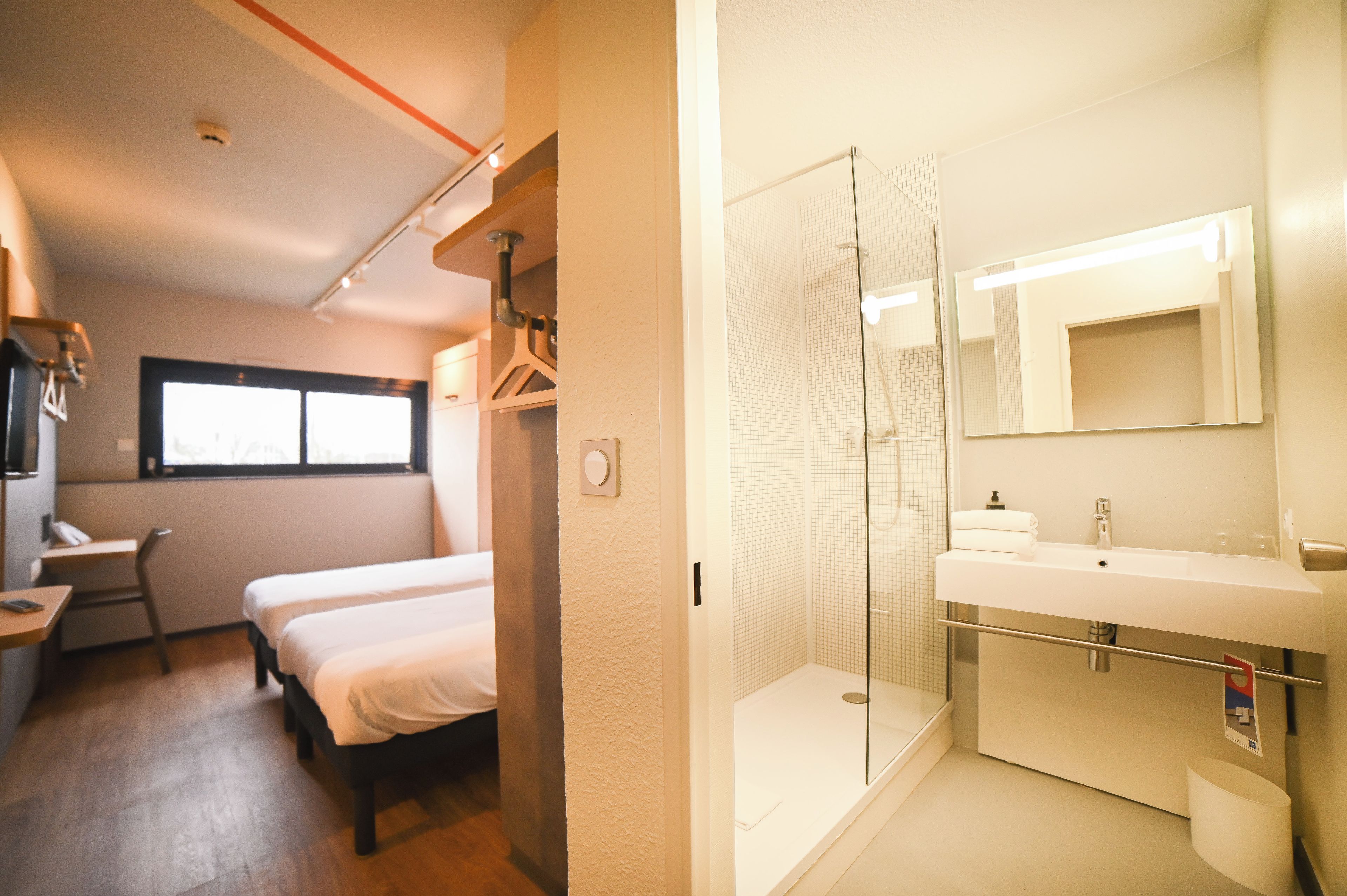 Une chambre d’hôtel comprenant un lit, un bureau, une chaise, une fenêtre et une salle de bain avec douche et lavabo.