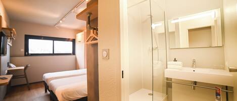 Habitación de hotel con cama, escritorio, silla, ventana y baño con ducha y lavamanos.