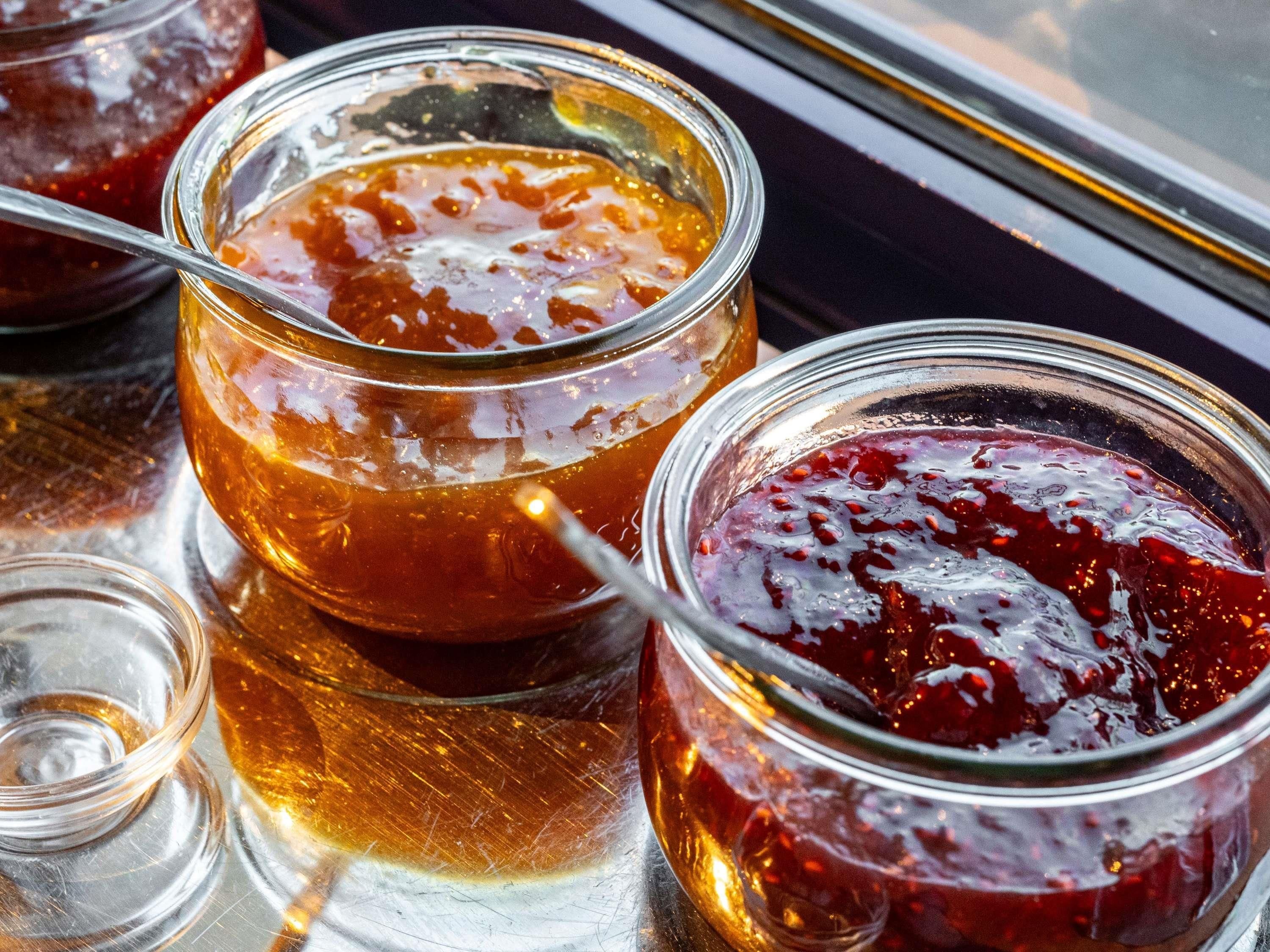 Three glass jars with a golden liquid and a red substance, possibly jam or honey, on a reflective surface.