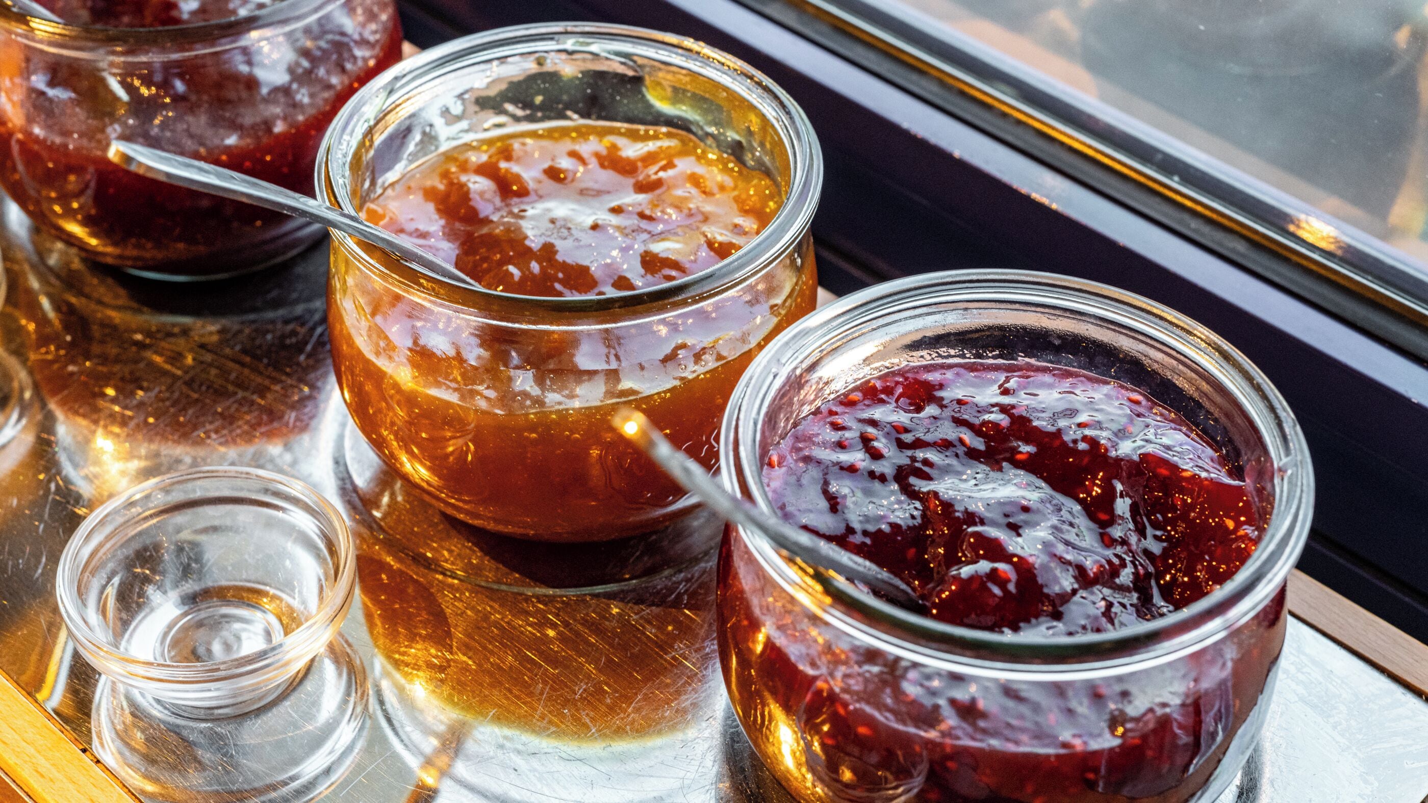Three glass jars with a golden liquid, possibly honey, on a reflective surface.