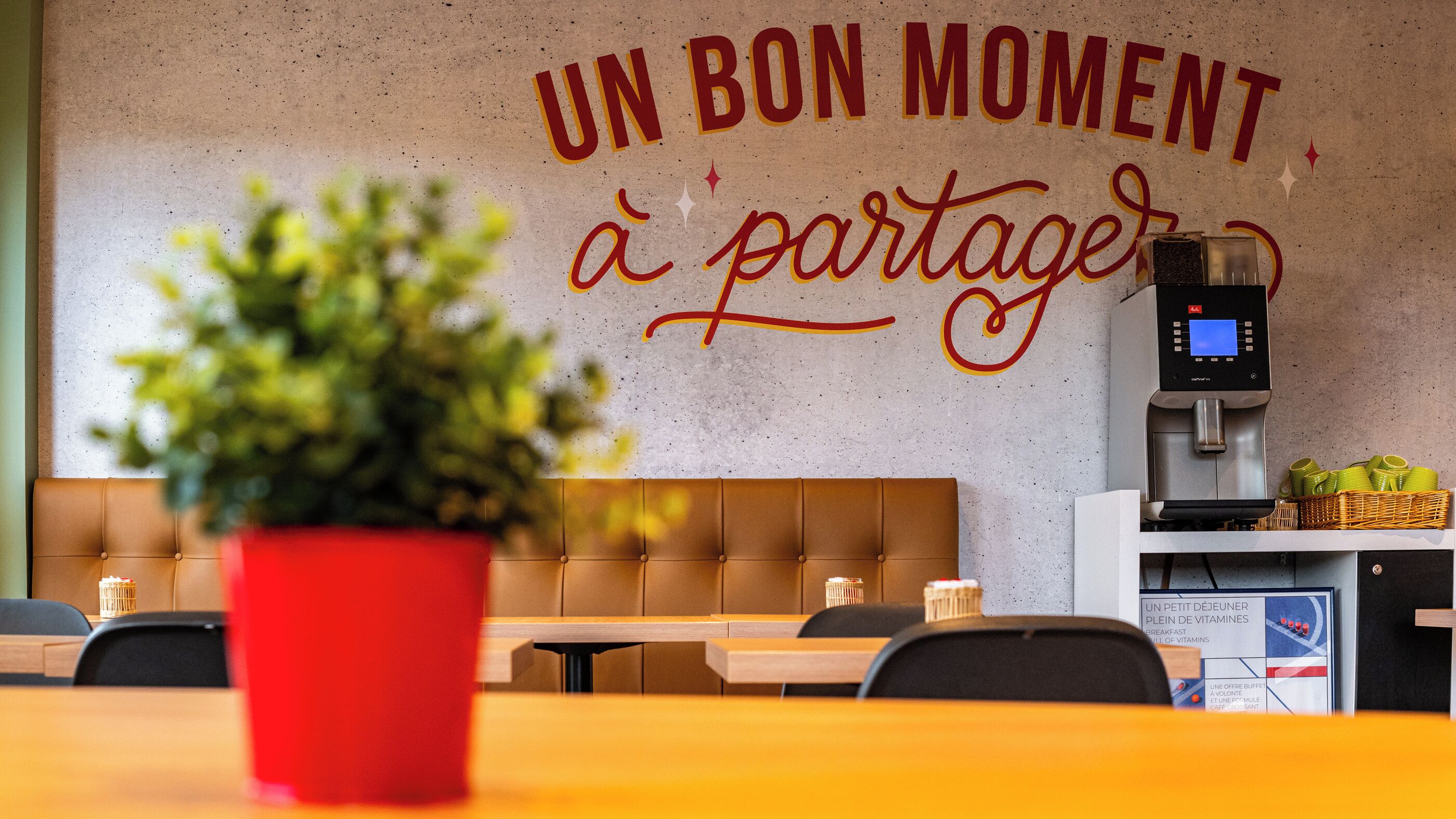 Interior de una cafetería con un letrero en la pared que dice 'UN BON MOMENT à partager' y una máquina de café.