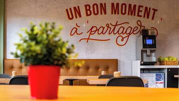 Interior de una cafetería con un letrero en la pared que dice 'UN BON MOMENT à partager' y una máquina de café.