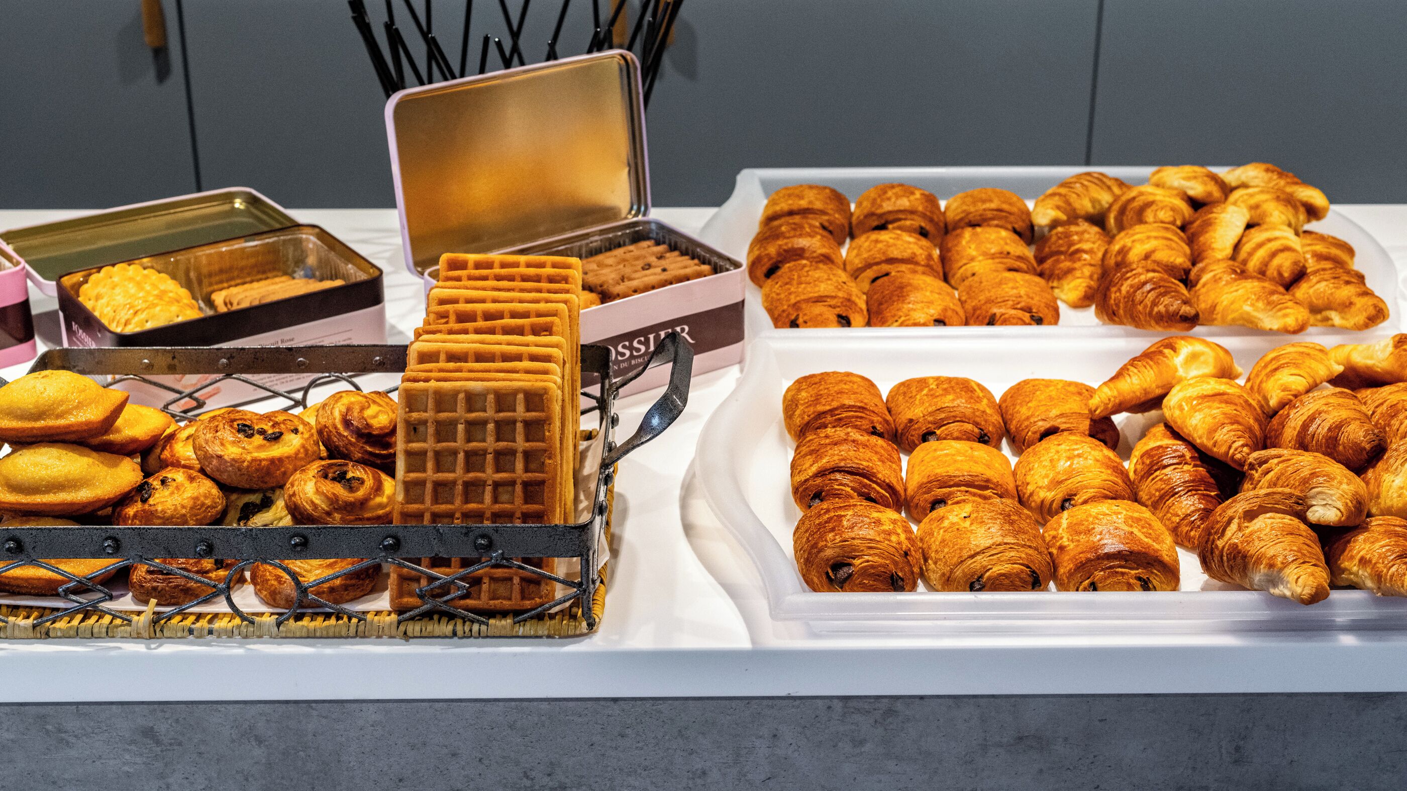 Une table de buffet proposant une variété de produits de boulangerie, notamment des gaufres, des pâtisseries et des croissants.