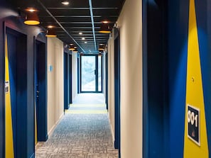 A corridor with doors numbered 001 and 004, leading to a bright exit. - Ibis Budget Reims Thillois (Thillois)