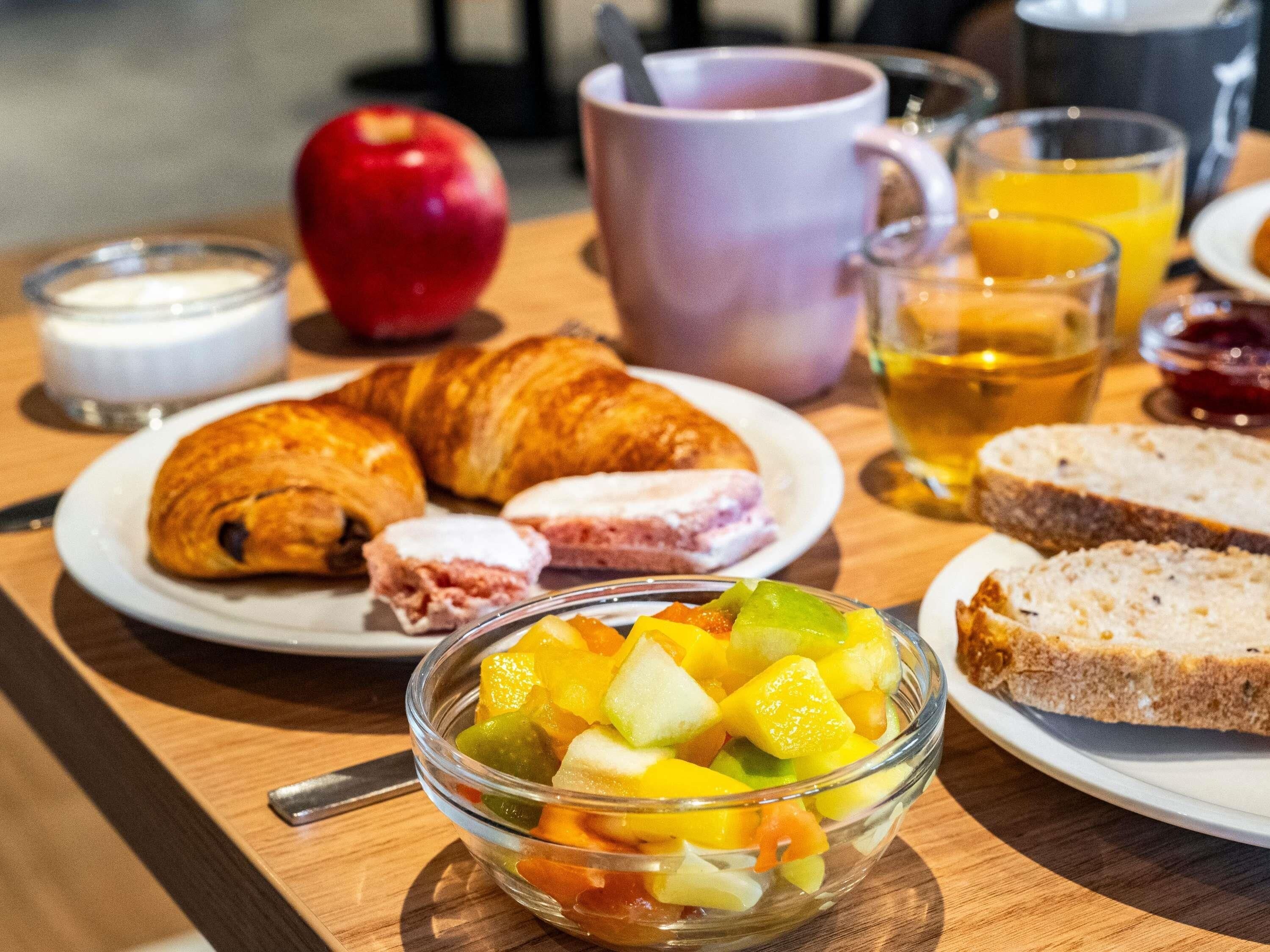 A breakfast setting with croissants, fruit, and beverages on a wooden table.