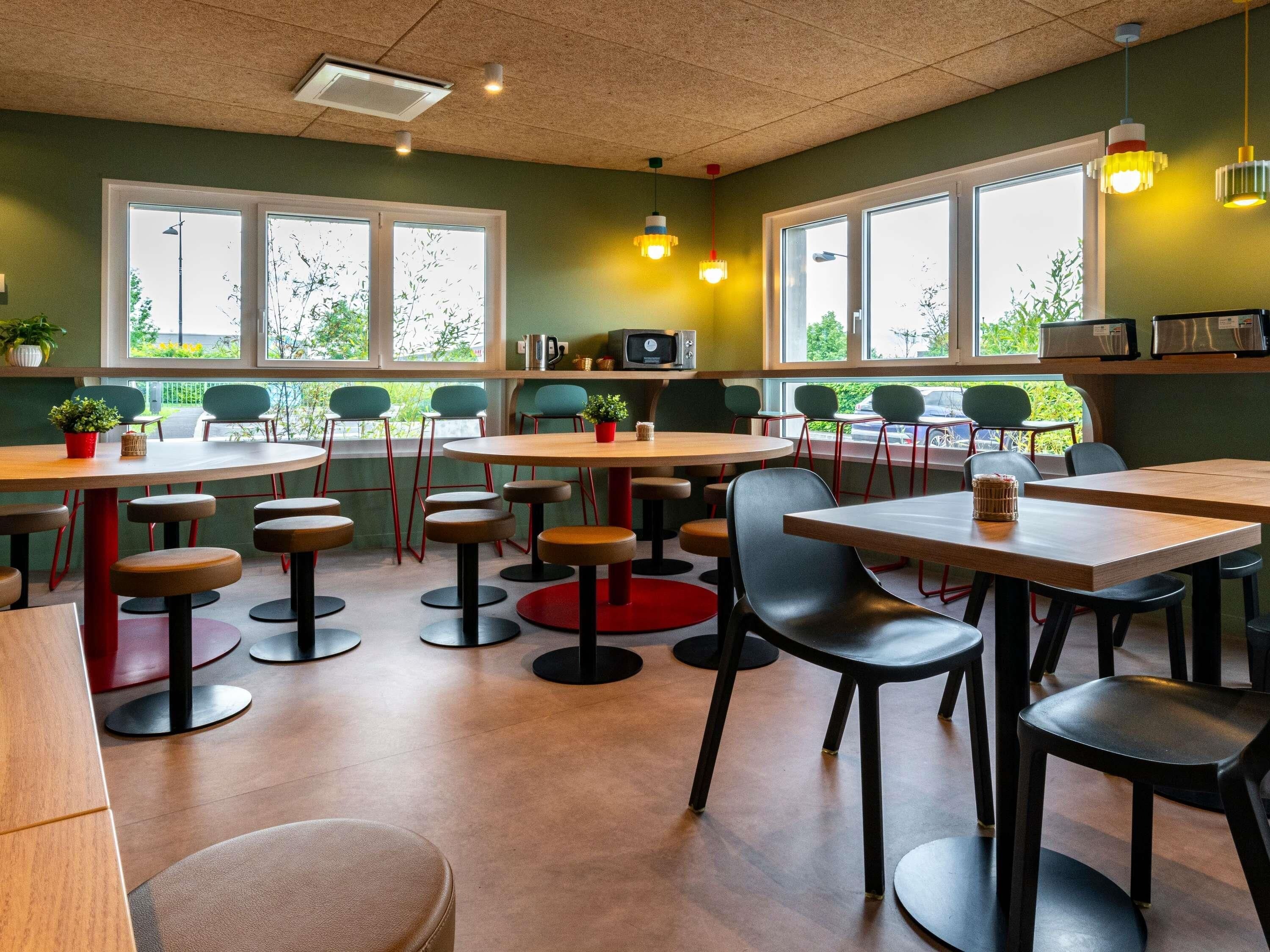 A modern cafe with multiple tables and chairs, large windows, and a ceiling with recessed lighting.