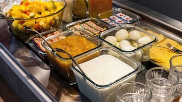 Un buffet proposant divers plats, notamment une salade de fruits, un pichet de jus d’orange et plusieurs autres mets.