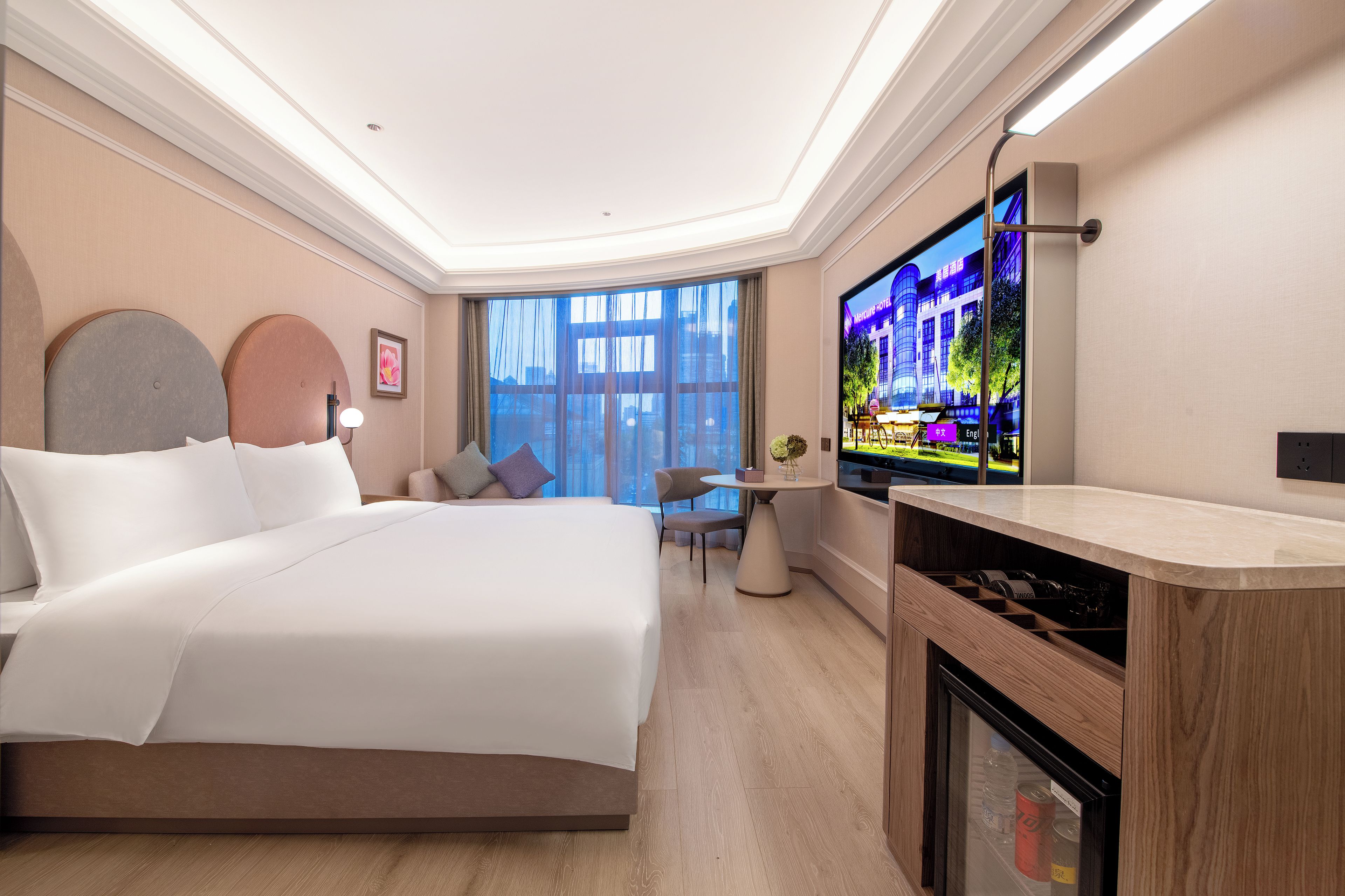 Una habitación de hotel moderna con una cama grande, un escritorio pequeño, televisión y vistas a la ciudad.