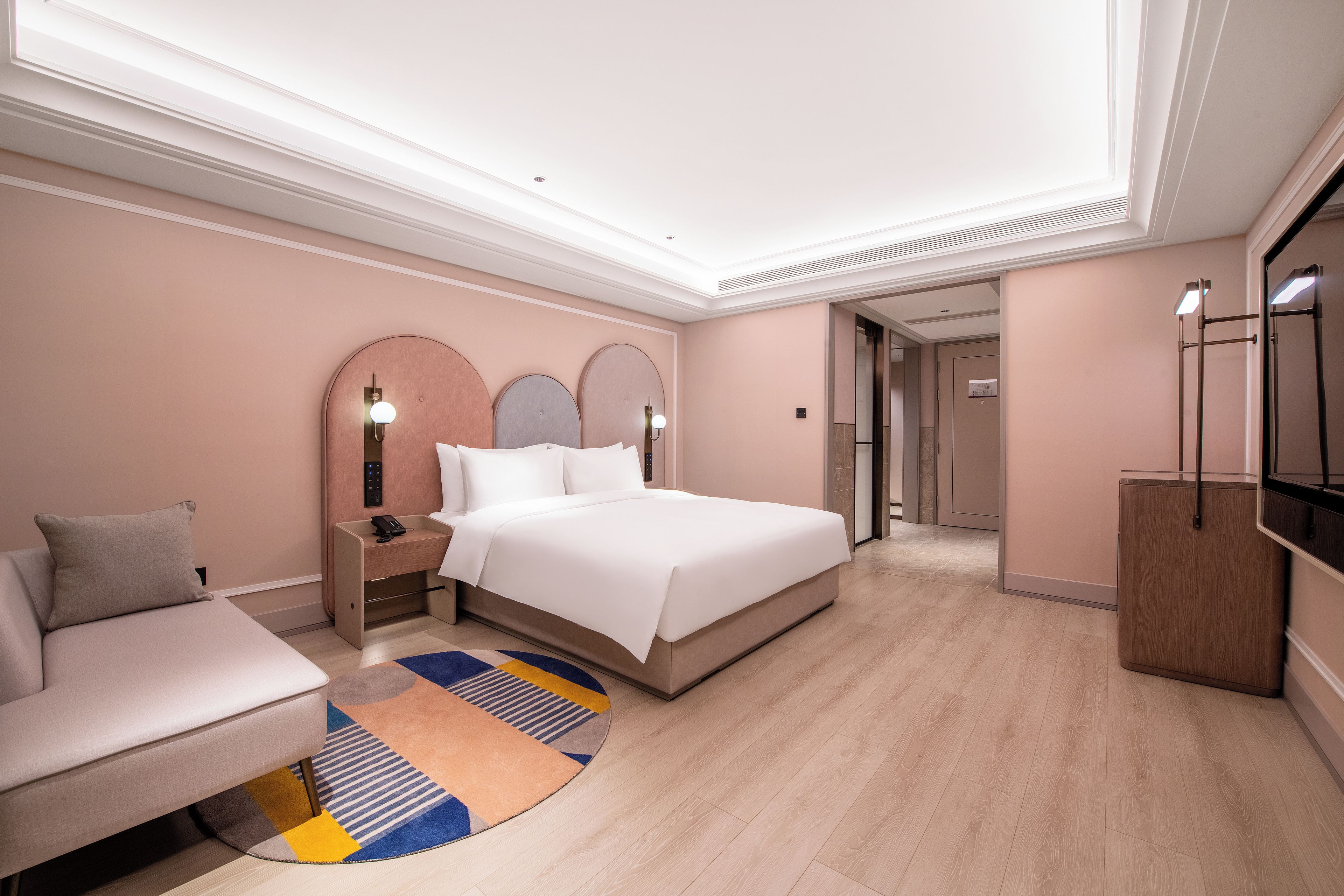 A modern hotel room with a large bed, bedside tables, a sofa, and a TV.