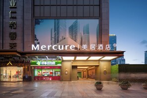 A hotel entrance with a large sign, a storefront with a green sign, and a view of tall buildings in the background. - Mercure Chengdu Chunxi Road Tianfu Square (Chengdu)