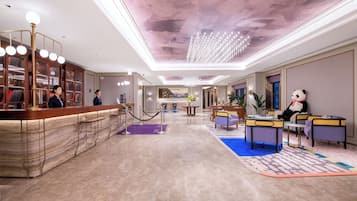 Un vestíbulo de hotel con recepción, zona de bar, arreglos de asientos y un peluche de panda.