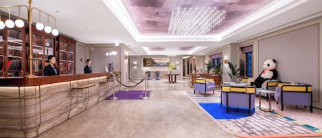 Eine Hotelhalle mit Empfangsschalter, Barbereich, Sitzgelegenheiten und einem Panda-Plüschtier.