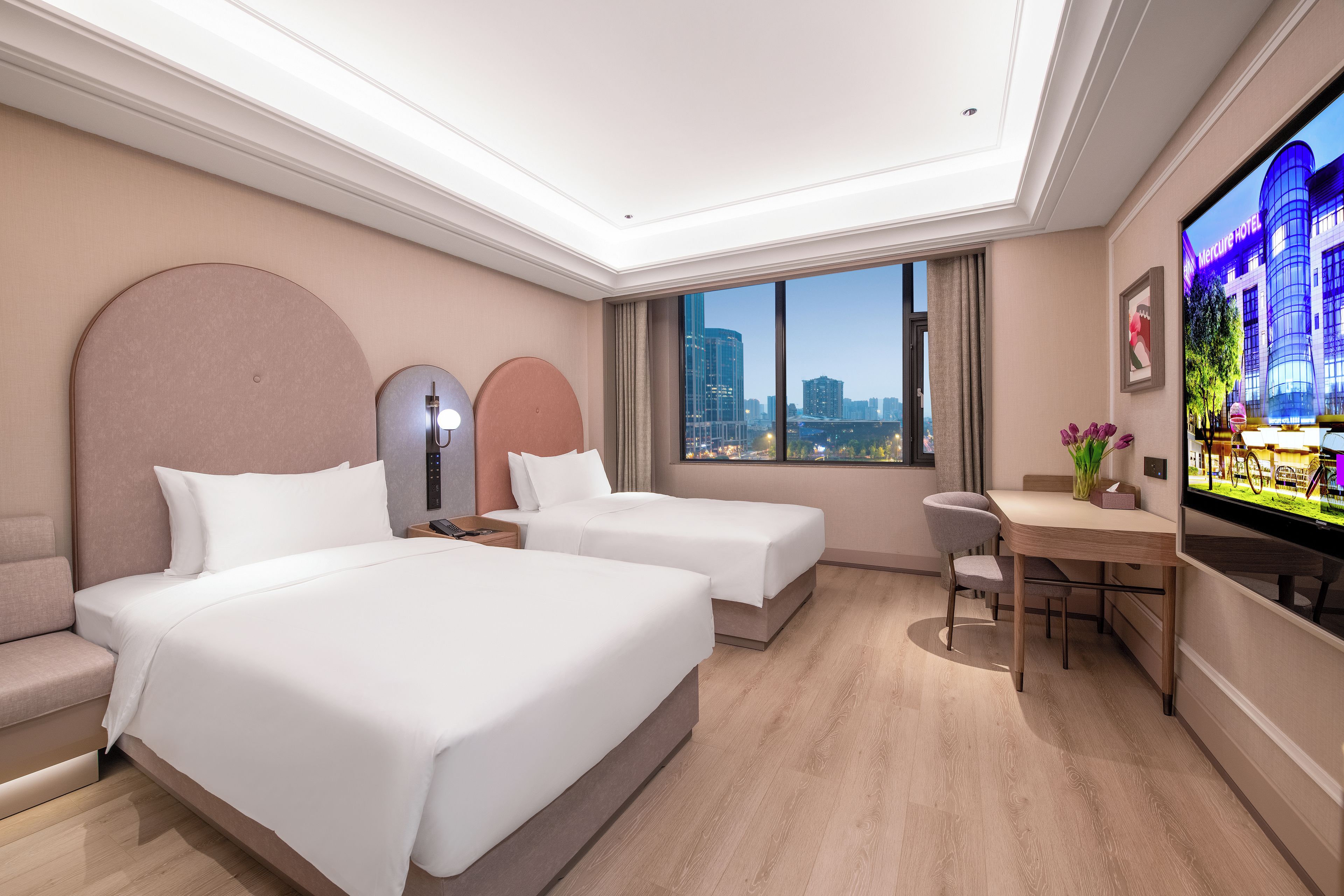 Habitación de hotel con dos camas, un escritorio, una silla, un televisor y vistas a la ciudad.