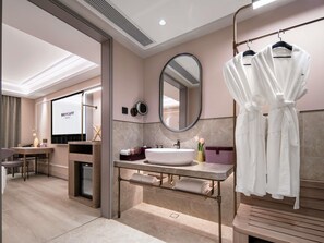 A modern bathroom with a vanity, mirror, and robe hooks.