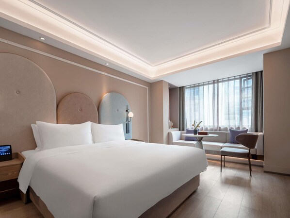 A modern hotel room with a large bed, a seating area with a table, and a large window with curtains.