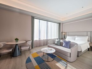 A modern hotel room with a bed, sofa, round table, and chairs. - Mercure Kunming Wujiaba (Kunming)