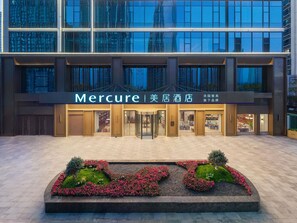 A hotel entrance with a modern facade, large glass windows, and a well-maintained garden area in front. - Mercure Kunming Wujiaba (Kunming)