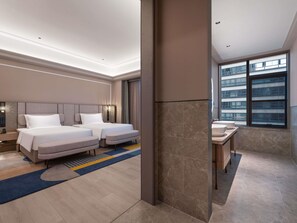 Habitación de hotel con dos camas, baño con ventanal grande y vista a la ciudad.