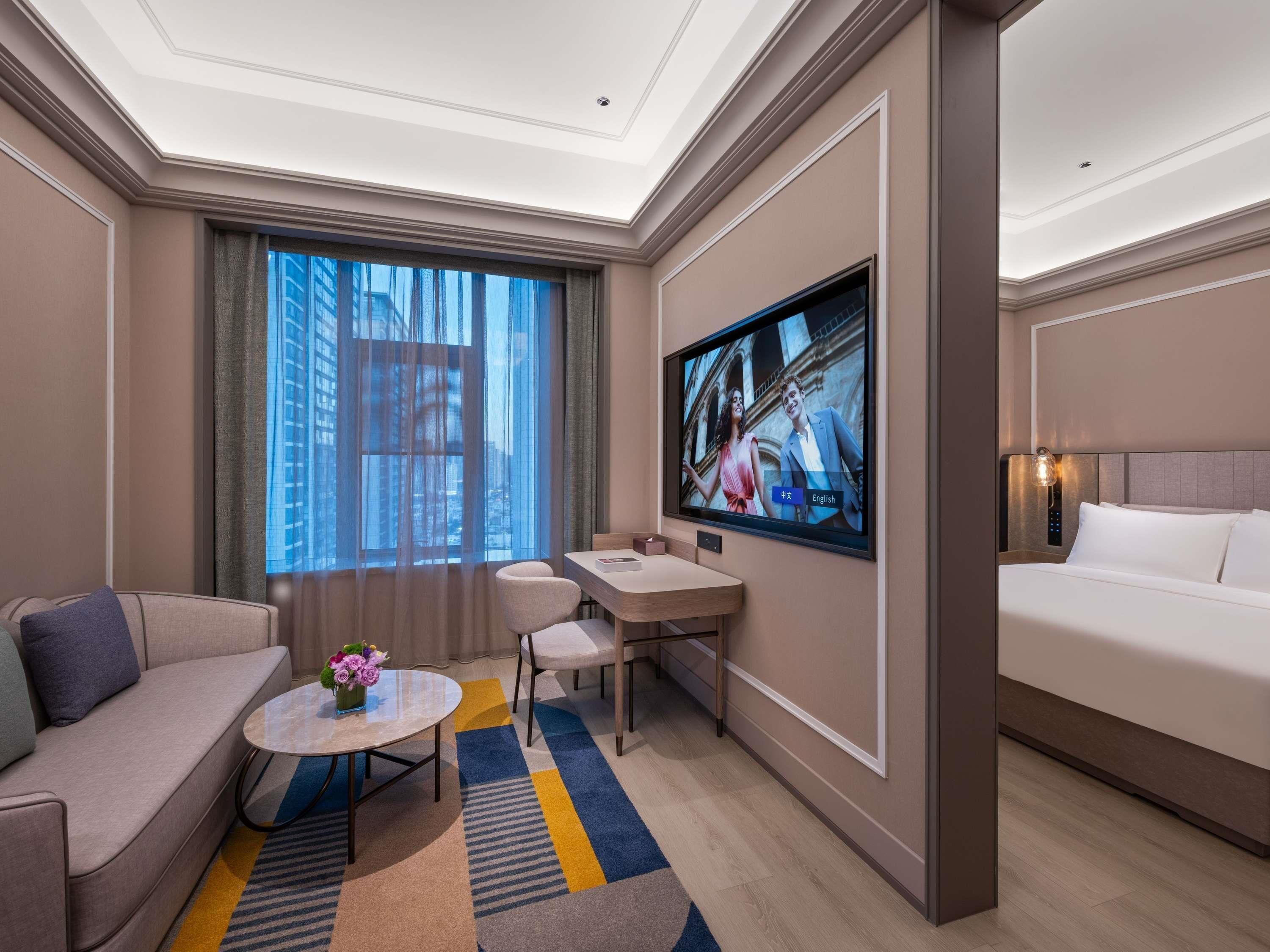 A hotel room with a bed, a desk, a sofa, a TV, and a window with curtains.