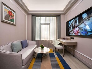 Habitación de hotel con sofá, una mesita redonda, televisor y ventana con cortinas.