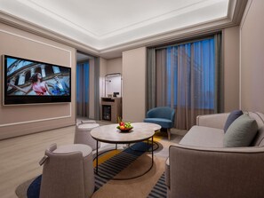 A hotel room with a flat-screen TV, a round coffee table with fruit, a sofa, and a chair. - Mercure Kunming Wujiaba (Kunming)