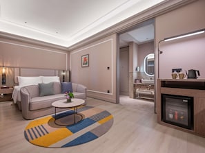 Habitación de hotel moderna con cama, sofá, mesa de centro y baño visible a través de una puerta abierta.