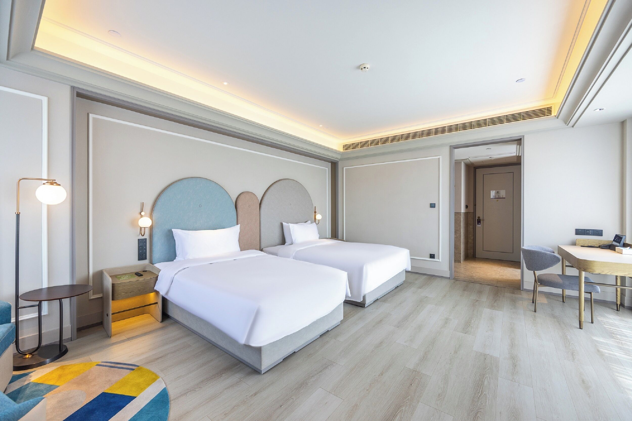 A hotel room with two beds, a desk, and a chair.