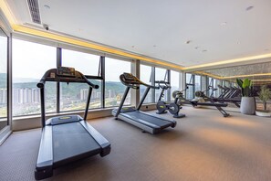 Un gimnasio con cintas de correr, bicicletas estáticas y máquinas de remo, amplias ventanas con vista a la ciudad y un diseño interior moderno.