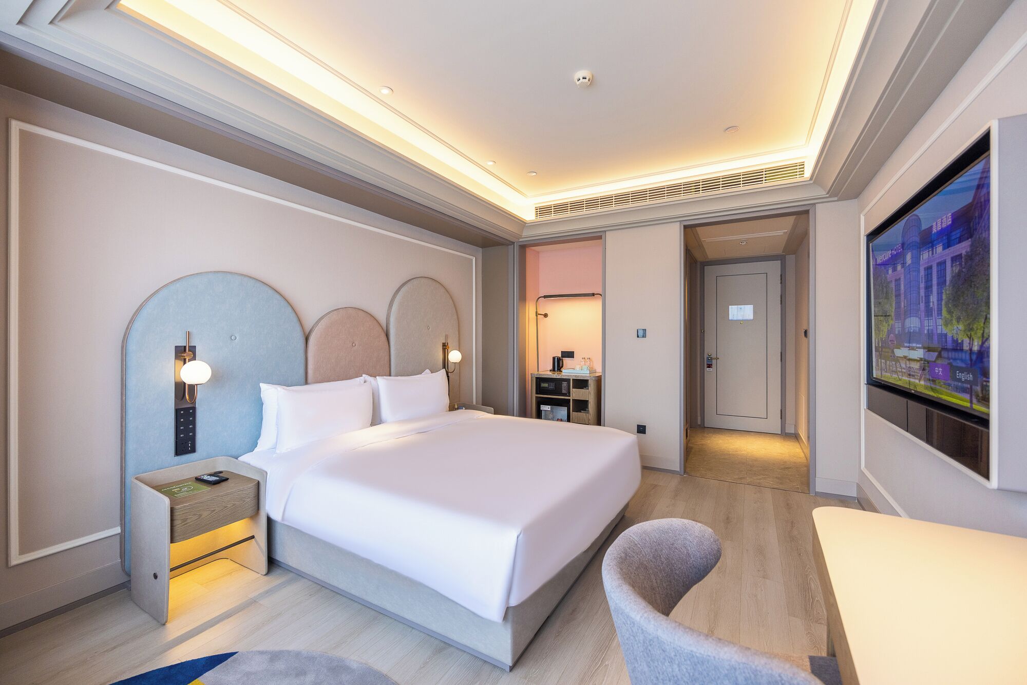 A hotel room with a large bed, bedside tables, a TV, and a view of the city.