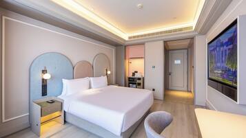 A hotel room with a large bed, bedside tables, a TV, and a view of the city.