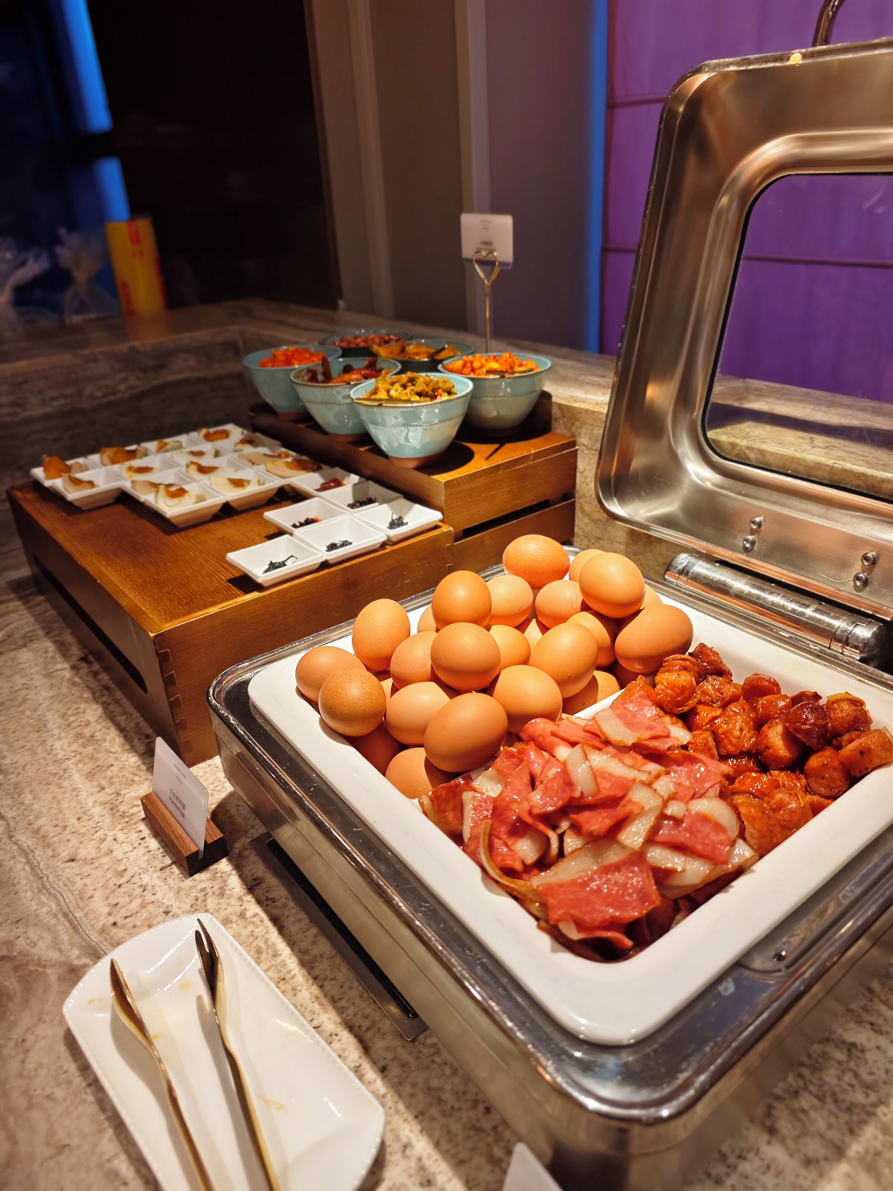 Una barra de desayuno con distintos alimentos como huevos, carnes y verduras.