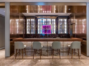 A bar area with a marble countertop, three bar stools, and a display of bottles behind glass panels.