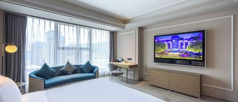 A hotel room with a large bed, a desk, a TV, and a sofa.