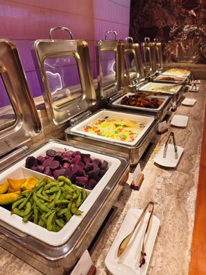 Un bufé con diversas opciones de comida, incluyendo batatas, judías verdes y un plato de verduras.