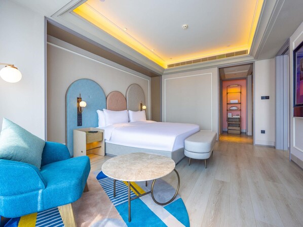 Una habitación de hotel moderna con cama, mesitas de noche, una mesa redonda, un sofá y un vestidor.