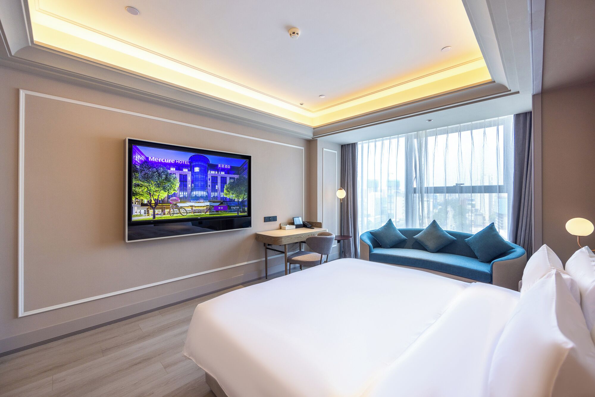 A hotel room with a bed, a desk, a chair, a television, and a large window with curtains.