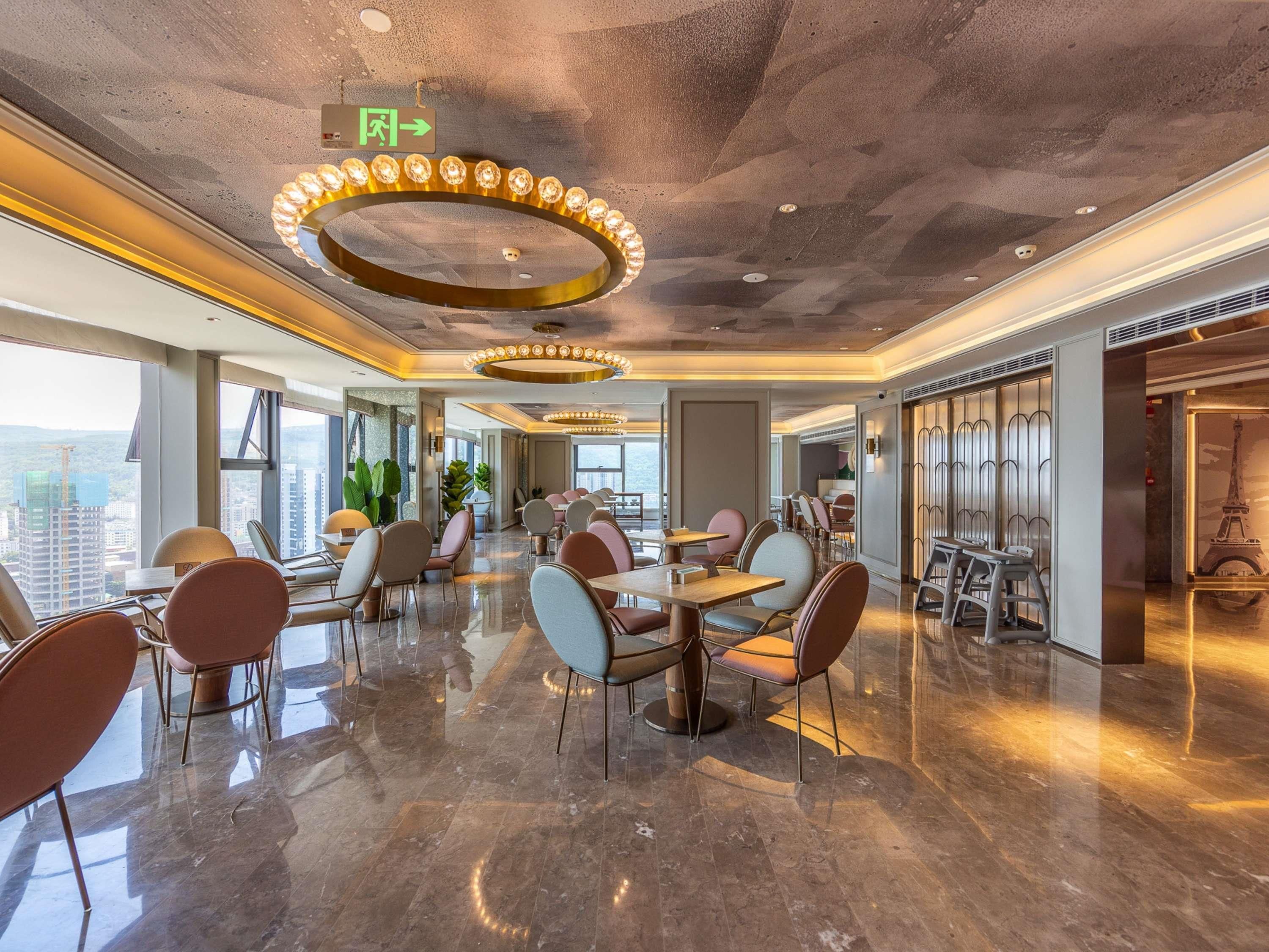 Un vestíbulo de hotel moderno con techo alto, pisos de mármol pulido y un accesorio de iluminación circular en el centro.