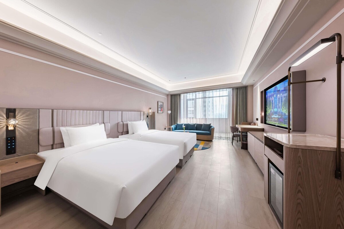 Una habitación de hotel con dos camas, un televisor, un escritorio y un ventanal grande.