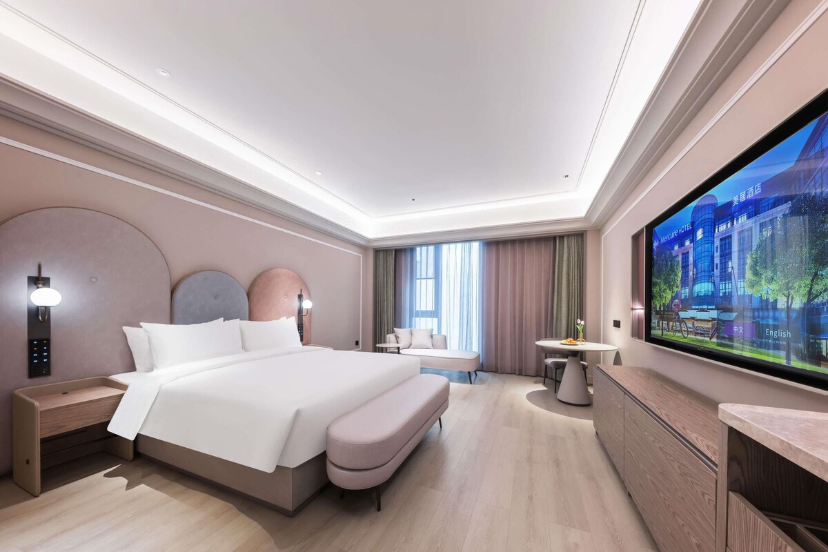 Una habitación de hotel moderna con una cama grande, mesitas de noche, televisión y una zona de estar.