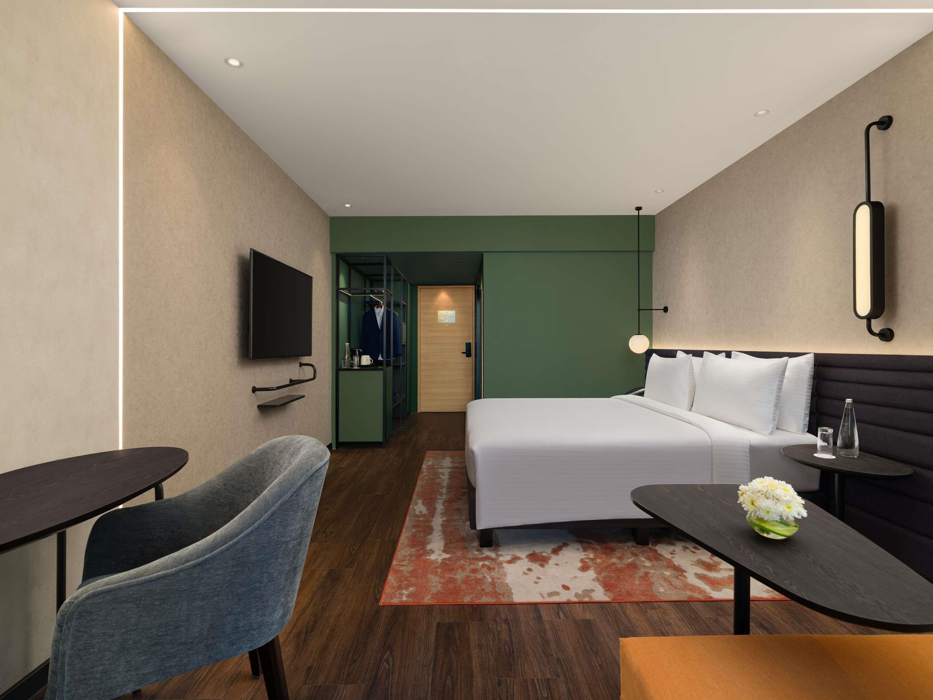 A hotel room with a bed, a desk, a chair, a TV, and a wardrobe.