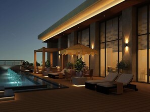 Un área de piscina en la azotea con sillones y una pérgola, rodeada de amplios ventanales y arquitectura moderna.