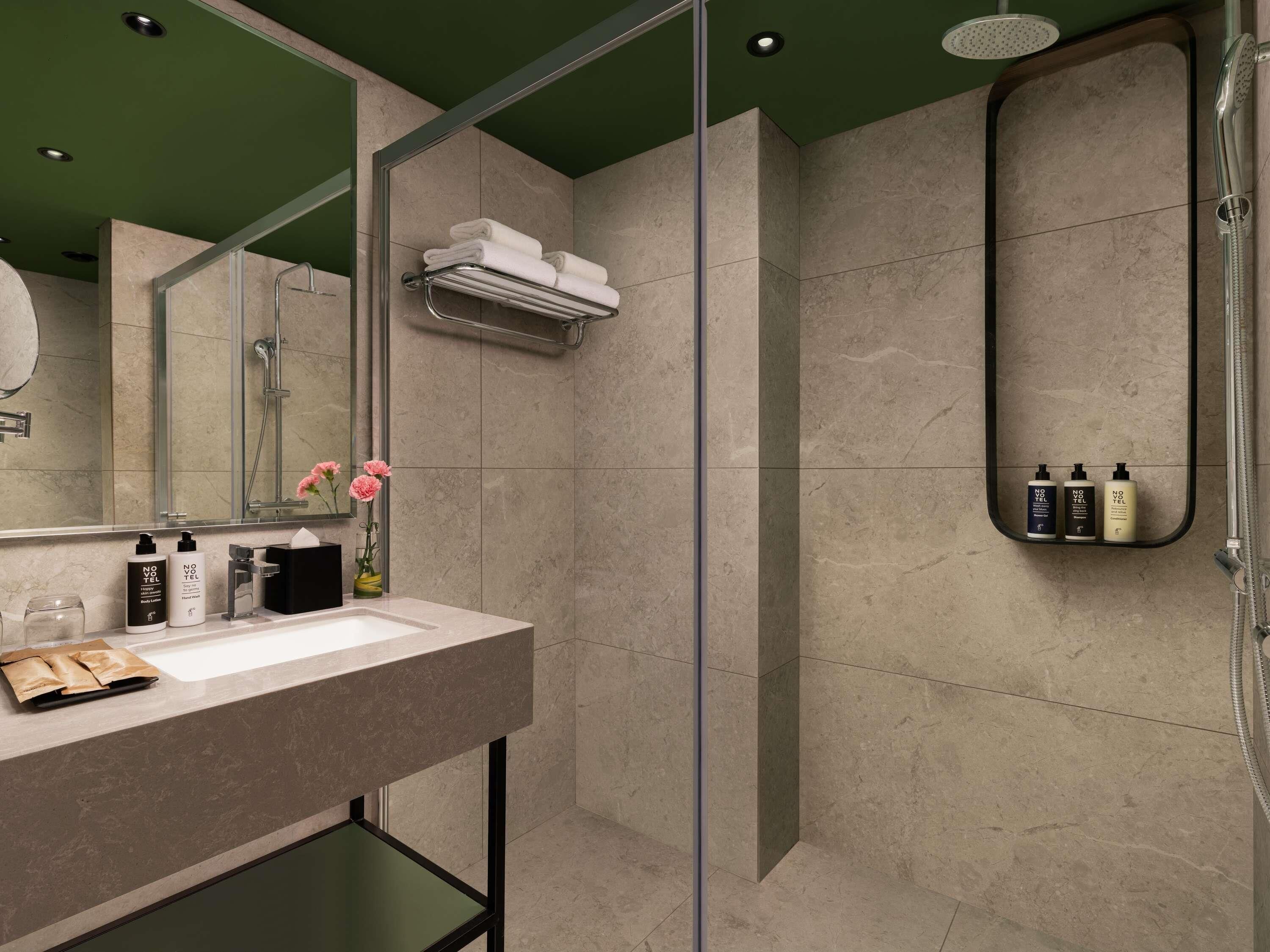 Un baño moderno con cabina de ducha de vidrio, tocador con espejo y artículos de aseo.