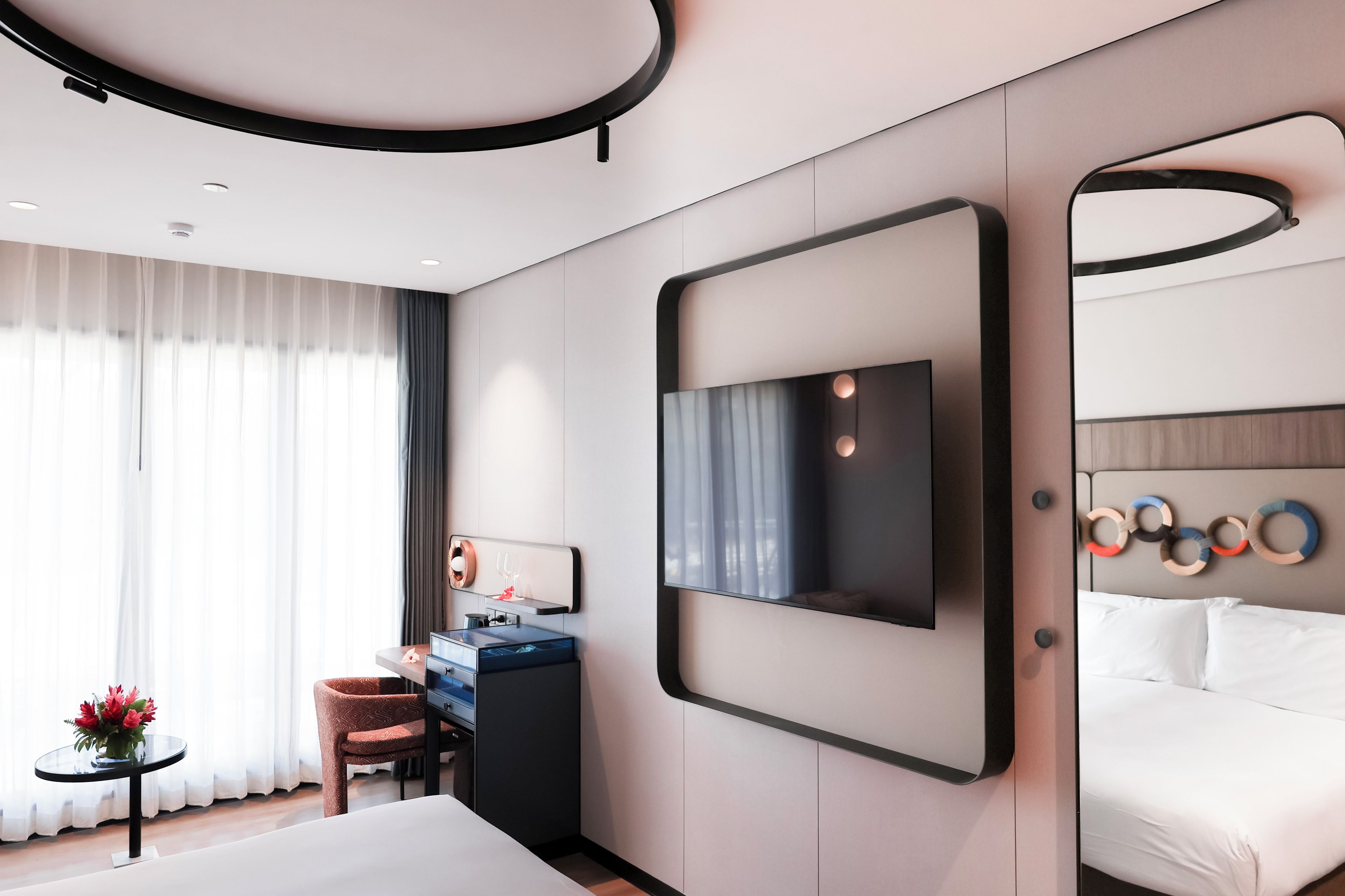 Habitación de hotel moderna con cama, escritorio con silla, espejo grande y televisor montado en la pared.