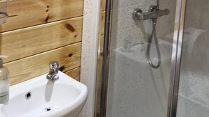 Een badkamer met een houten wand, een douchecabine van glas, een witte wastafel en een hangspiegel.
