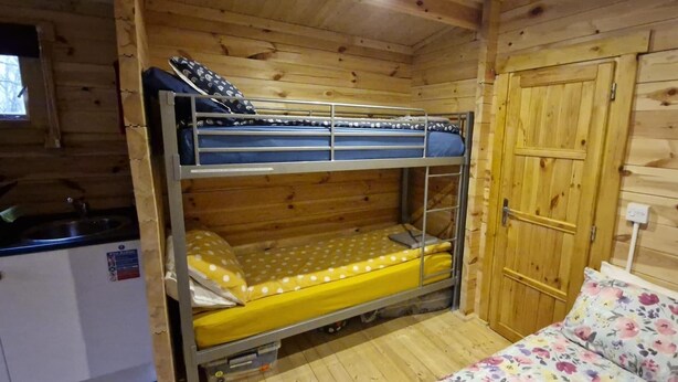 A bunk bed with a lower bunk, a wooden door, a small kitchenette, and a window. - Muntjac Lodge dog Friendly nr Anderby Creek (Alford)