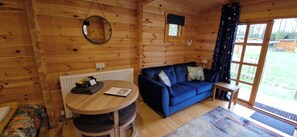 Ein gemütliches Zimmer mit Holzvertäfelung, einem runden Tisch mit einem Buch, einem blauen Sofa mit Kissen und einem Fenster mit Vorhängen.