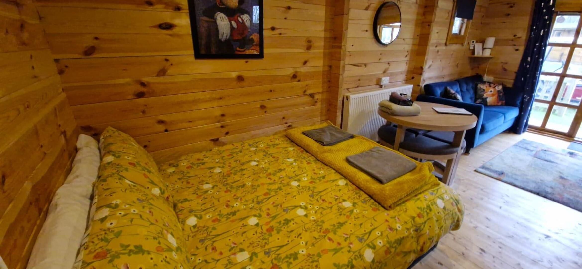 A wooden cabin room with a bed, a round table, and a blue sofa.
