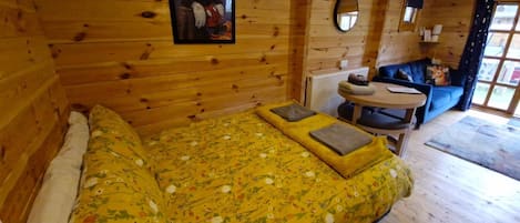 A wooden cabin room with a bed, a round table, and a blue sofa.